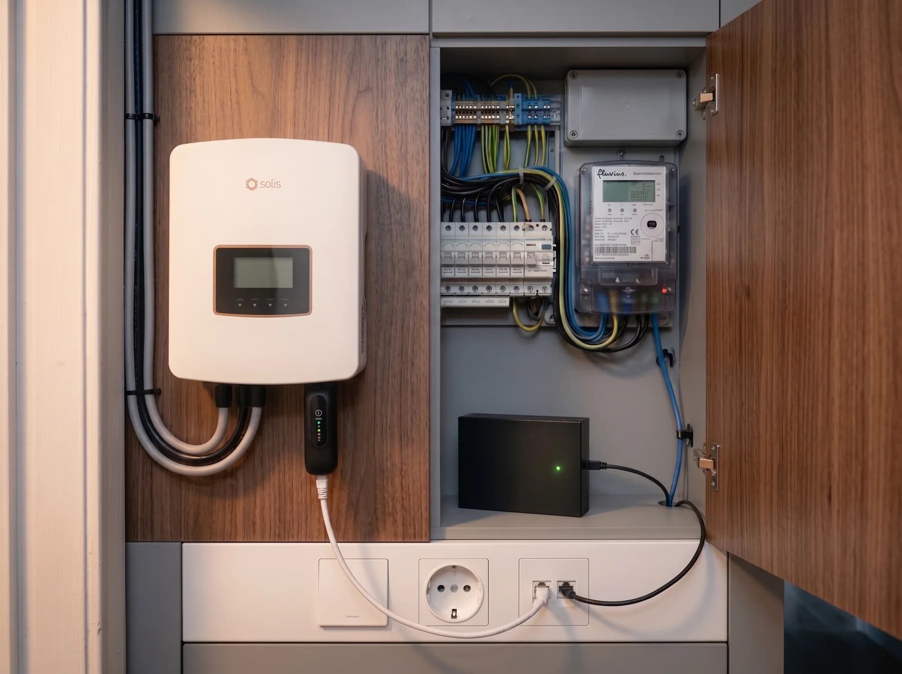 Een meterkast met een witte Solis-omvormer, de Fluvius digitale meter en de zwarte Novolt-box met een groen lampje.